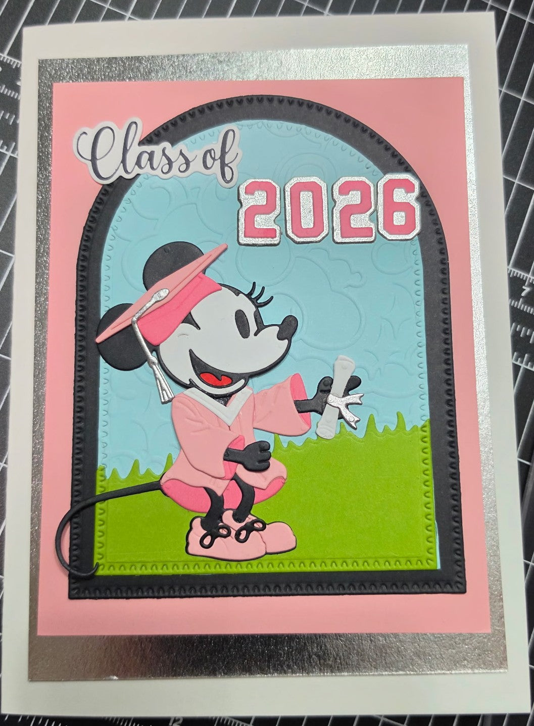 Graduation-themed card with cartoon character and 'Class of 2026' text on a checkered background.